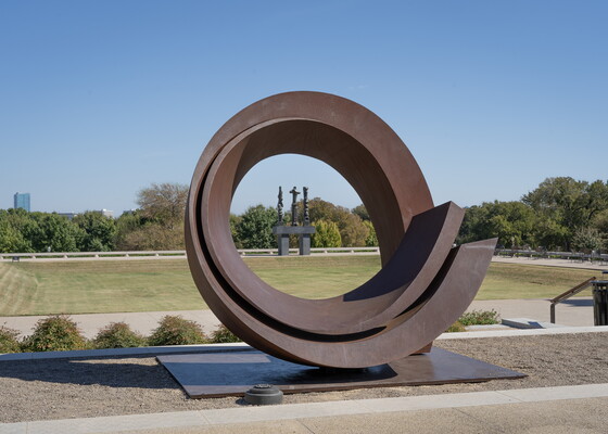 A large rusted steel sculpture that takes the form of a curlicue on its side.