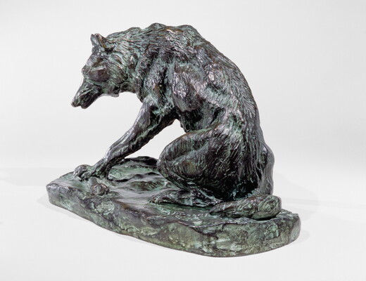 A bronze sculpture of a wolf crouching on its haunches.