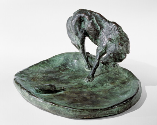 A bronze sculpture of a wolf staring at a bottle on the ground.