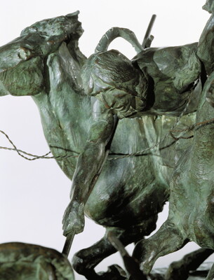 A detail of a bronze sculpture of two horses in mid-gallop, with both riders lunging toward a crouching man behind a shield.