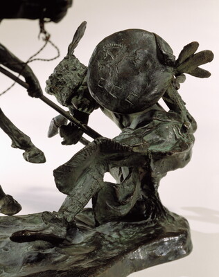 A detail of a bronze sculpture of two horses in mid-gallop, with both riders lunging toward a crouching man behind a shield.