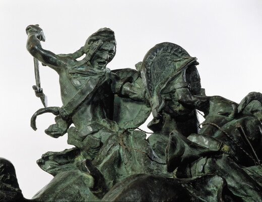 A bronze sculpture of two horses in mid-gallop, with both riders lunging toward a crouching man behind a shield.