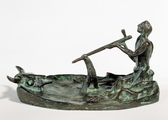 A bronze sculpture of a kneeling Native American man smoking a pipe in front of a bison skull.