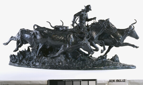A bronze sculpture of a cowboy on a running horse surrounded by stampeding cattle.