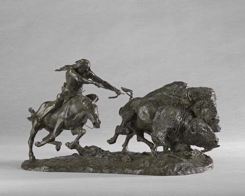 A sculpture of a Native American on horseback using a bow and arrow to hunt two bison.