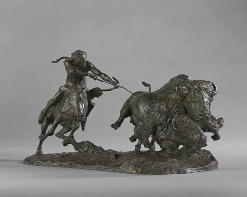 A sculpture of a Native American on horseback using a bow and arrow to hunt two bison.