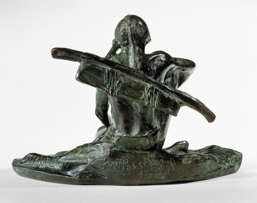 A bronze sculpture with a slight green patina of an Indigenous man seated on the ground.