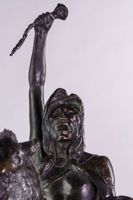 A detail of a bronze sculpture of a man on horseback holding a piece of scalp and hair in his hand thrusted above his head triumphantly.