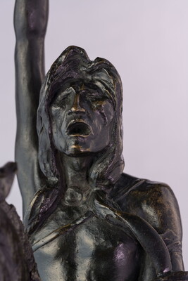 A detail of a bronze sculpture showing the face of a man on horseback holding a piece of scalp and hair in his hand thrusted above his head triumphantly.