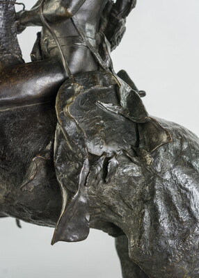 A detail of a bronze sculpture showing saddle of a man on horseback holding a piece of scalp and hair in his hand thrusted above his head triumphantly.