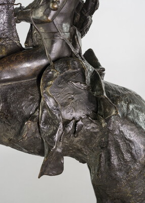 A detail of a bronze sculpture showing saddle of a man on horseback holding a piece of scalp and hair in his hand thrusted above his head triumphantly.