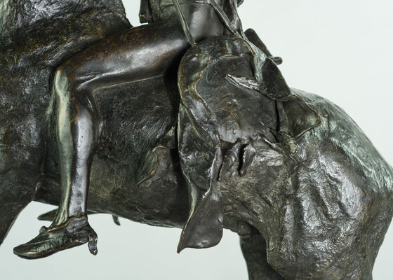 A detail of a bronze sculpture showing saddle of a man on horseback holding a piece of scalp and hair in his hand thrusted above his head triumphantly.