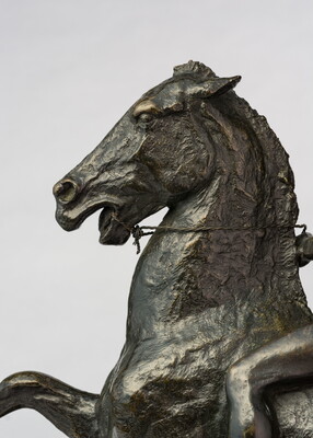 A detail of a bronze sculpture showing the head of the horse of a man on horseback holding a piece of scalp and hair in his hand thrusted above his head triumphantly.