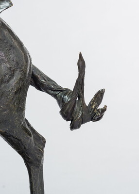 A detail of a bronze sculpture showing the tail of the horse of a man on horseback holding a piece of scalp and hair in his hand thrusted above his head triumphantly.