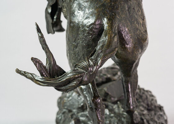 A detail of a bronze sculpture showing the rear of the horse of a man on horseback holding a piece of scalp and hair in his hand thrusted above his head triumphantly.