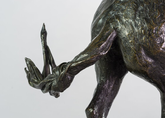 A detail of a bronze sculpture showing the tail of the horse of a man on horseback holding a piece of scalp and hair in his hand thrusted above his head triumphantly.