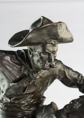 A bronze sculpture of a cowboy balancing on a rearing horse.
