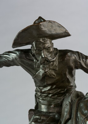 A bronze sculpture of a cowboy balancing on a rearing horse.