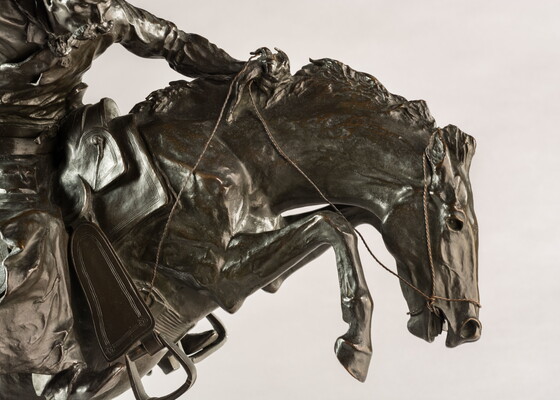 A bronze sculpture of a cowboy balancing on a rearing horse.