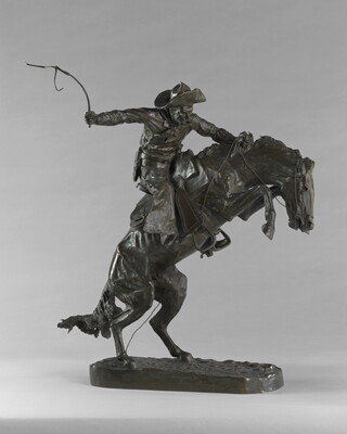 A bronze sculpture of a cowboy balancing on a rearing horse.