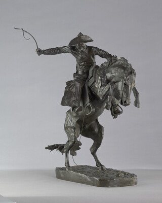 A bronze sculpture of a cowboy balancing on a rearing horse.