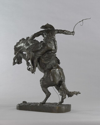 A bronze sculpture of a cowboy balancing on a rearing horse.