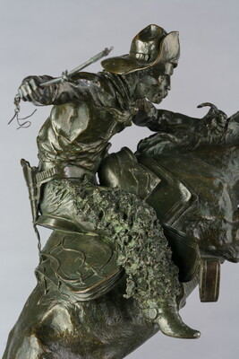 A detail of bronze sculpture of a cowboy balancing on a rearing horse.