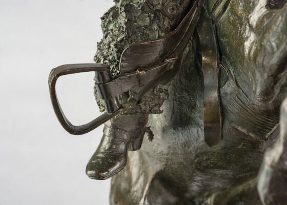 A detail of bronze sculpture of a cowboy balancing on a rearing horse.