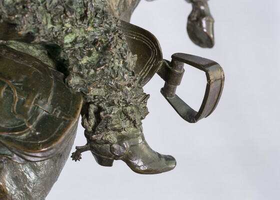 A detail of bronze sculpture of a cowboy balancing on a rearing horse.