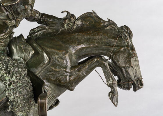 A detail of bronze sculpture of a cowboy balancing on a rearing horse.