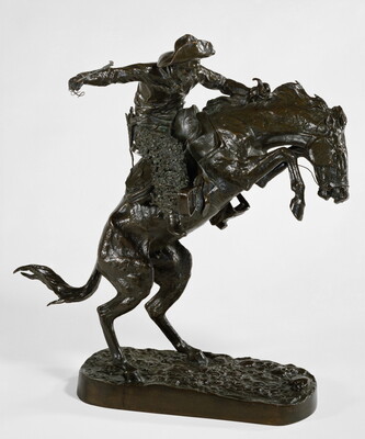 A bronze sculpture of a cowboy balancing on a rearing horse.
