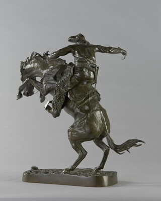 A bronze sculpture of a cowboy balancing on a rearing horse.