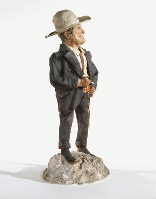 A painted sculpture of a man wearing a cowboy hat, a light-colored shirt, and dusty pants and jacket standing on a rock, smoking a cigarette.