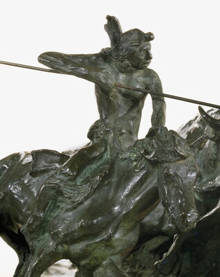 A detail of a bronze sculpture of two Native men, one with a spear and the other with a bow, on horseback circling a group of bison.