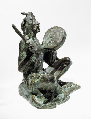 A bronze sculpture of a sitting Indigenous man playing a handheld drum.