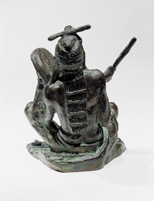 A bronze sculpture of a sitting Indigenous man playing a handheld drum.