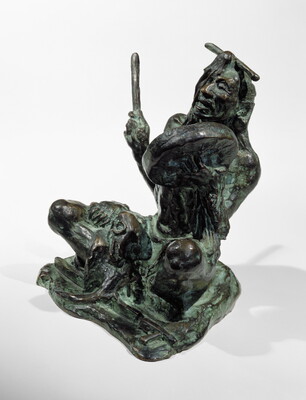 A bronze sculpture of a sitting Indigenous man playing a handheld drum.