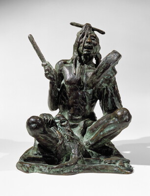 A bronze sculpture of a sitting Indigenous man playing a handheld drum.