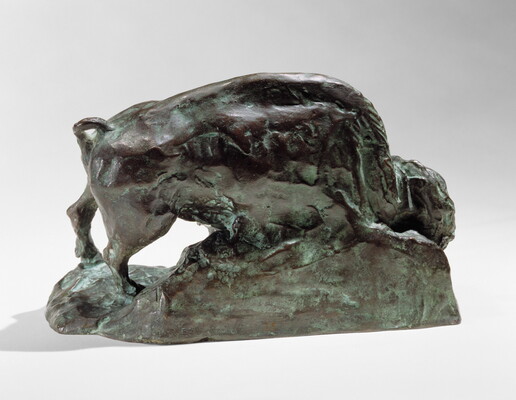 A bronze sculpture of a bison with his head and front leg lowered toward the ground.