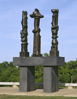 Three tall, vertical, bronze sculptures of organic forms atop a geometrically carved base.