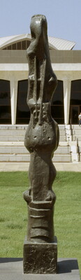 A tall, vertical, bronze sculpture of organic forms atop a geometrically carved base.