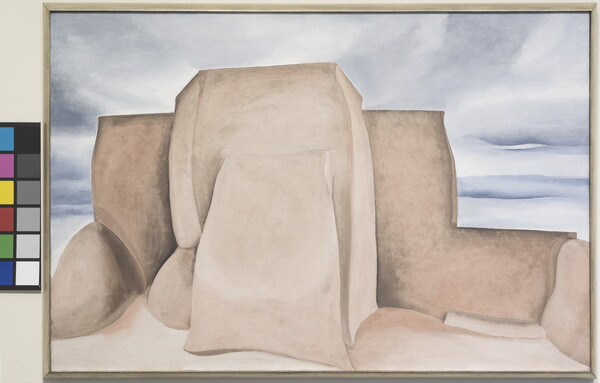 An oil painting of the back of a large adobe structure set against a muted blue sky.