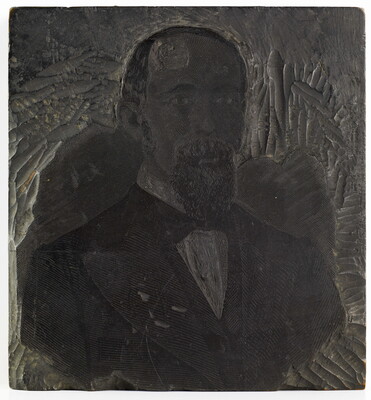 A metal printing block with a portrait of the head and shoulders of a balding man with a goatee wearing a suit.
