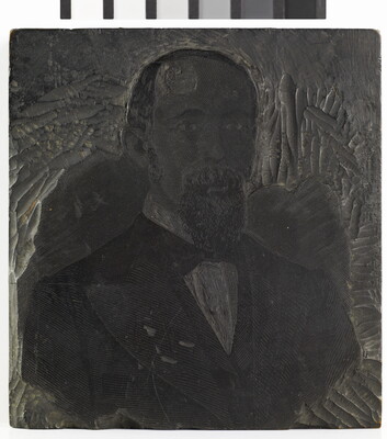 A metal printing block with a portrait of the head and shoulders of a balding man with a goatee wearing a suit.
