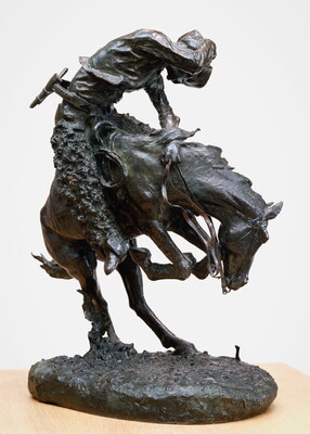 A bronze sculpture of a cowboy riding a bucking horse around a rattlesnake.