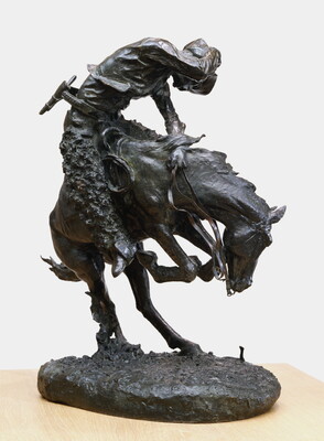 A sculpture of a man riding a bucking horse around a rattlesnake.