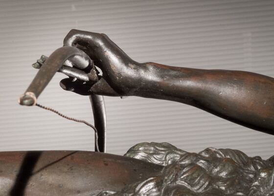 A detail of bronze sculpture of a young man holding a bow and arrow, standing hunched low with a dog beside him.