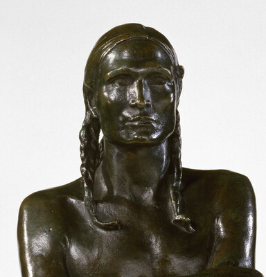 A detail of a bronze sculpture of a Native American man who stands wrapped in a blanket.