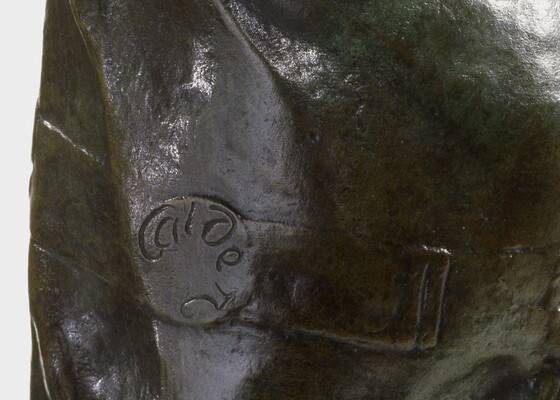 A detail of a bronze sculpture of a Native American man who stands wrapped in a blanket.