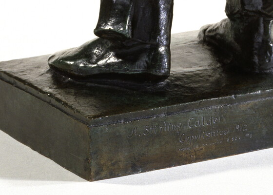 A detail of a bronze sculpture of a Native American man who stands wrapped in a blanket.